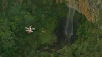A rescue helicopter hovers above a waterfall near where a man fell to his death on the Gold Coast.