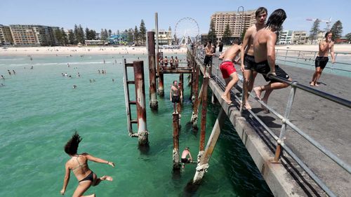 Teens jump of the jetty at Glenelg beach during a hot day in Adelaide.