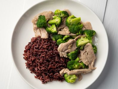Cooked riceberry rice and Stir fried broccoli with pork tenderloin fillet in white plate.