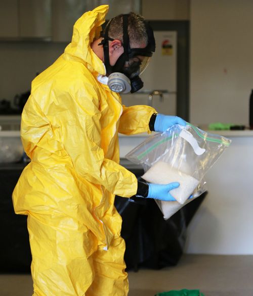 A forensic officer wearing a full containment suit, including mask, handles some drugs. (Supplied)