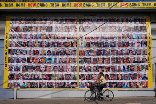 A woman cycles next to a billboard calling for the return of about 240 hostages who were abducted during the Oct. 7, Hamas attack on Israel. in Tel Aviv, Israel on Friday, Nov. 24, 2023.