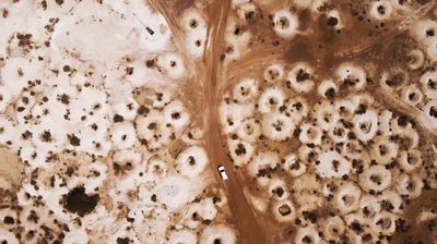Aerial of a car driving through the outback town of White Cliffs.