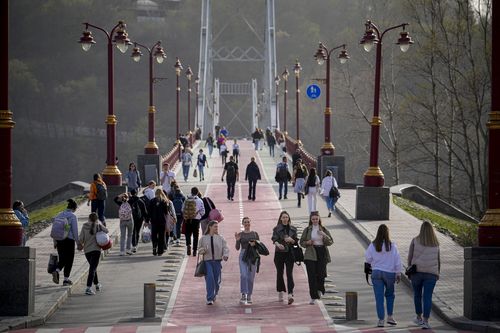 People cross a bridge on a warm afternoon on the bank of the Dniepr River in Kyiv, Ukraine, Tuesday, April 2, 2024. 