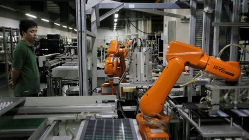 A Chinese man works amid orange robot arms at Rapoo Technology factory in southern Chinese industrial boomtown of Shenzhen. (AAP)