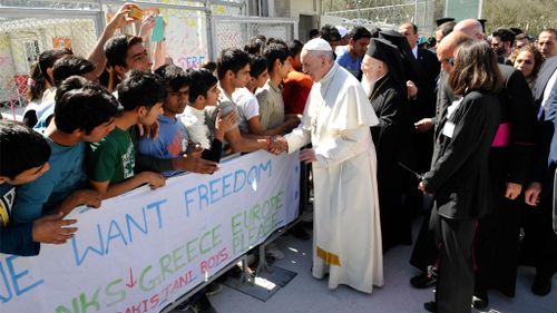 Pope Francis, center, and Ecumenical Patriarch Bartholomew I, greet migrants and refugees during a visit on the Greek island of Lesbos. (AAP)