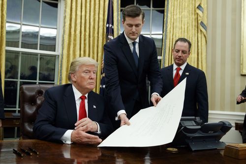 Rob Porter (middle) hands a document to President Donald Trump in the Oval Office. (AAP)