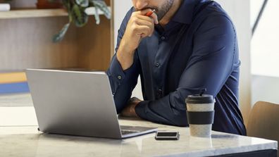 Serious mid adult professional looking at laptop. Confident businessman working at desk. He is concentrating in office.