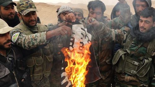 Syrian Army soldiers burning an ISIL flag. (AAP)