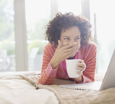 Woman covering her smile and holding a coffee mug