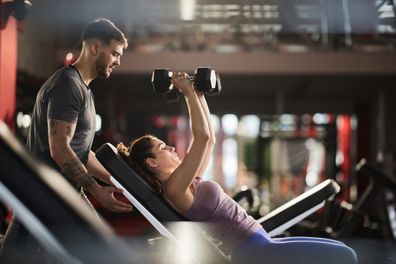 Fitness instructor assisting athletic woman in exercising with dumbbells at gym.