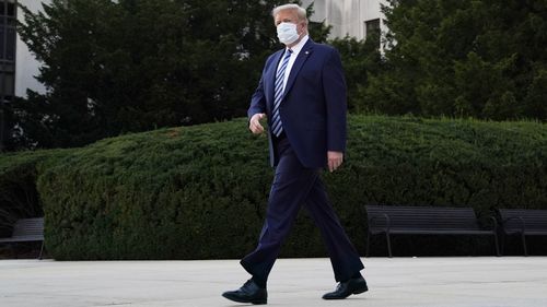 A masked Donald Trump walks out of the hospital this morning.