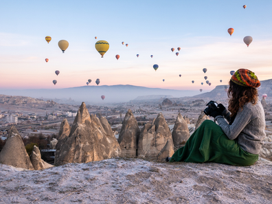 Young women (solo traveller) shooting photos of hot air balloons flying in red and rose valley in Goreme in Cappadocia in Turkey stock photo