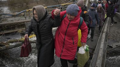 Des femmes se tiennent la main en traversant la rivière Irpin sur un chemin improvisé sous un pont qui a été détruit par une frappe aérienne russe, tout en aidant les personnes fuyant la ville d'Irpin, en Ukraine, le samedi 5 mars 2022. Ce qui ressemblait à un cessez-le-feu révolutionnaire pour L'évacuation des habitants de deux villes d'Ukraine s'est rapidement effondrée samedi, les responsables ukrainiens ayant déclaré que les bombardements avaient interrompu les travaux d'évacuation des civils quelques heures après l'annonce de l'accord par la Russie.  (AP Photo/Vadim Ghirda)