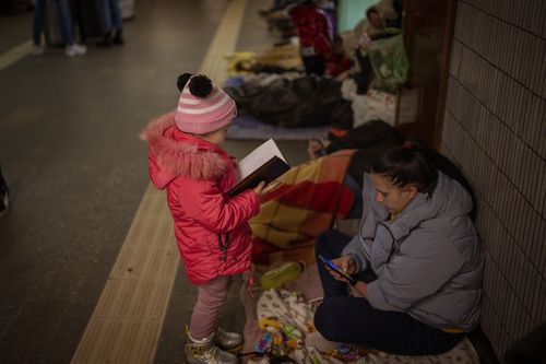 A girl looks at a notebook next to her mother as they stand in the Kyiv subway, using it as a bomb shelter, Ukraine, Saturday Feb. 26, 2022. 