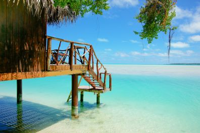 Steps down to over-water wooden landing on tropical island with view to horizon over turquoise water in island of Aitutaki.