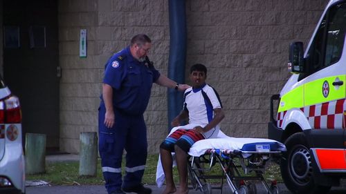 A NSW Ambulance worker comforts a man on a stretcher after two men drowned and one is still missing north of Coffs Harbour in NSW.