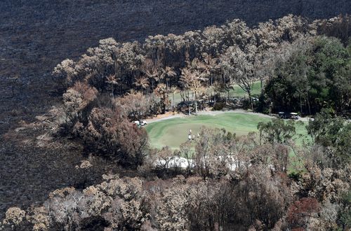 Golfers are seen on the green next to a bushfire-damaged area in Peregian beach on the Sunshine Coast. (AAP Image/Dan Peled)
