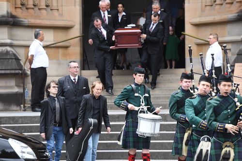 Angus Young, the brother of Malcolm Young, carries a guitar as he walks with Ross Young, the son of Malcolm Young, as they lead the casket of his brother Malcolm. (AAP)