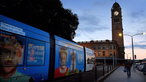 A man walks towards Central Station as a light rail train goes by in Sydney