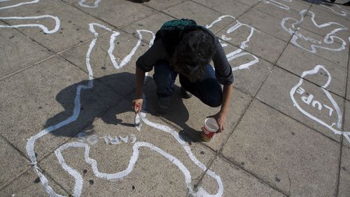 A woman paints the name of a victim of the Mexican drug war onto a body outline as part of a memorial for those killed, on the 10th anniversary of the drug war's start, at the Monument for the the Mexican Revolution, in Mexico City, in 2016