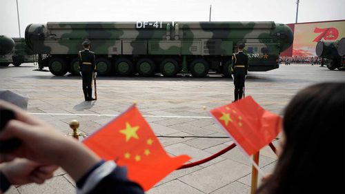 Spectators wave Chinese flags as military vehicles carrying DF-41 ballistic missiles roll during a parade.