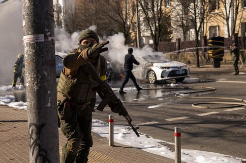 Ukrainian soldiers take positions outside a military facility as two cars burn, in a street in Kyiv, Ukraine, Saturday, Feb. 26, 2022. 
