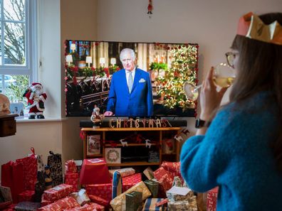 On his first Christmas Day broadcast to the nation since the death of his mother, Queen Elizabeth III in September, King Charles III speaks to a suburban family on their widescreen TV in their living room that is filled with wrapped presents, on 25th December 2022, in Nailsea, England 