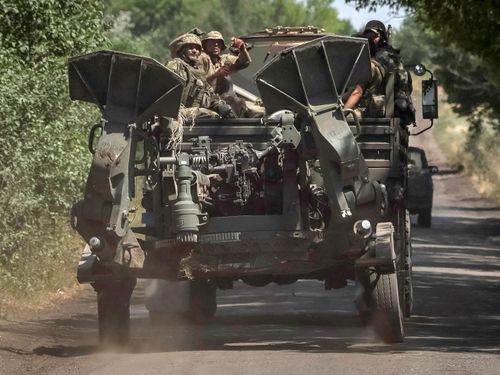 Ukrainian servicemen ride on a military vehicle as they tow an M777 howitzer near the front line, in the Donbas region.