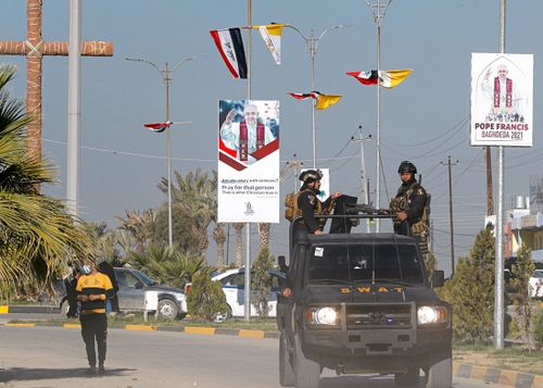 Iraqi security forces pass by Iraqi and Vatican flags and posters in a street in Qaraqosh, Iraq, Monday, Feb. 22, 2021, announcing the visit of the Pope Francis.