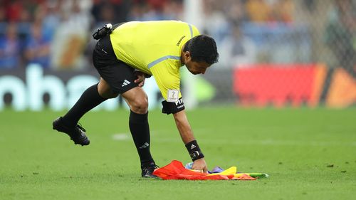 The referee picks up the abandoned  rainbow flag after a spectator invaded the field in the Portugal-Uruguay match.