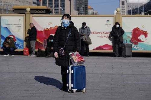 A traveller waits outside the Beijing Station with her suit case in Beijing, China, Friday, Jan. 28, 2022. 