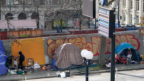 A person at left walks toward the entrance of a tent used by people experiencing homelessness, Tuesday, March 1, 2022, in downtown Seattle across the street from City Hall. 