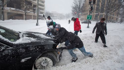 Pedestrians help push out a commuter's car during a major blizzard. (AAP)