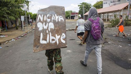  A young woman walks with a shield on his back with a message that reads 'Nicaragua Free' during the fifth day of protests in Managua, Nicaragua. (AAP)