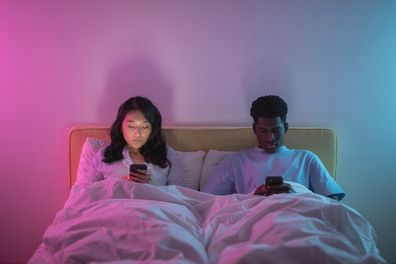 People sitting in a bed, texting, couple