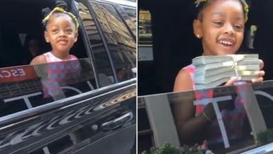 Cardi B and Offset's daughter Kulture standing at the window of a black SUV holding a large wad of cash.