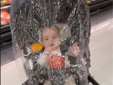 Baby in a pram with a rain protector on top while inside supermarket.