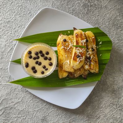 Grilled banana served with cheese sauce and chocolate chips on the white plate and placed on grey textured background. Selective focus image.