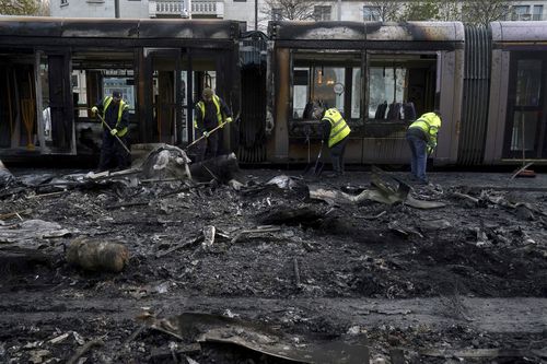 Debris is cleared from a burned out Luas and bus on O'Connell Street, in the aftermath of violence in the city center on Thursday evening, in Dublin, Friday, Nov. 24, 2023.  