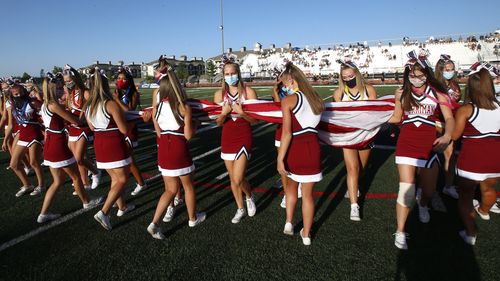 Herriman cheerleaders carry the American flag before the start of a high school football game between Davis and Herriman , in Herriman, Utah.