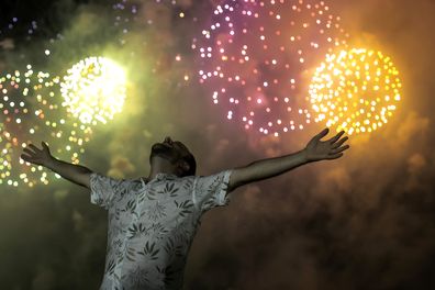 A man celebrates the start of the New Year, backdropped by fireworks exploding in the background over Copacabana Beach in Rio de Janeiro, Brazil, Saturday, Jan. 1, 2022.