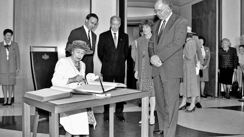 Her Royal Highness Queen Elizabeth II signs the visitors' book at Parliament House, while Prime Minister Paul Keating and Parliament House officials look on, February 1992.