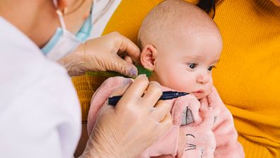 Enlarged photo of a little babygirl whose doctor point the place for medical earrings. Ear piercing for kids. Cropped photo. High quality photo
