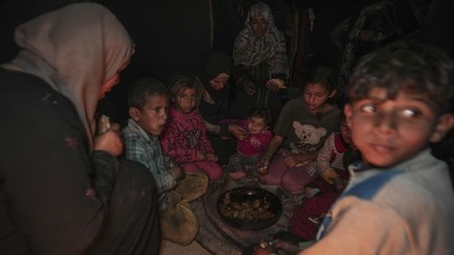 Amani Abu Zarada, fourth from left, feeds one of her children with fried zucchini made over a fire made of paper and cardboard scraps outside their tent in a camp in Khan Younis, Gaza Strip, Thursday, Dec. 19, 2024. (AP Photo/Abdel Kareem Hana)