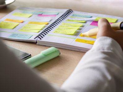 Close-up of agenda organize with color coding sticky notes for time management. Productive schedule for appointments and reminders. Hand holding a yellow highlighter marker. Organization and planning