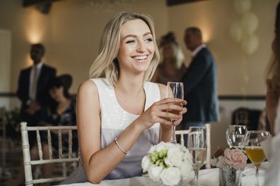 Young woman is sitting at a table at a wedding with a glass of champagne.