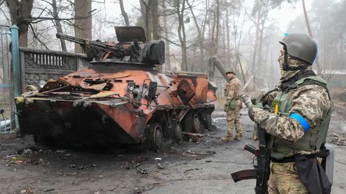 Ukrainian troops look at a damaged Russian tank near Kyiv.