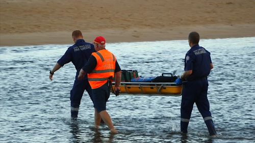 Emergency services carry a stretcher filled with medical gear through the shallows.