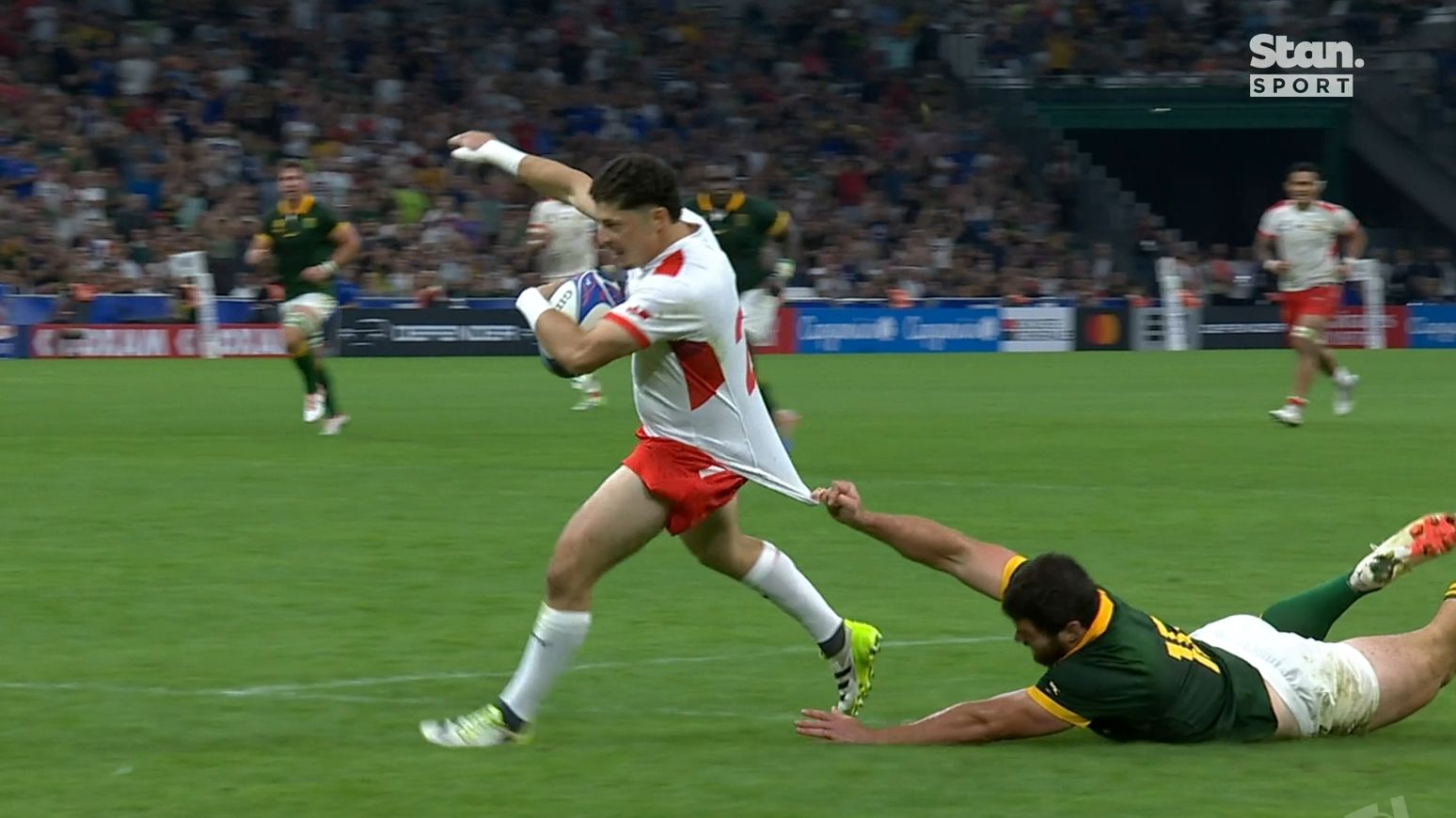 A South African player tries valiantly to stop Patrick Pellegrini from scoring Tonga&#x27;s final try of the match.
