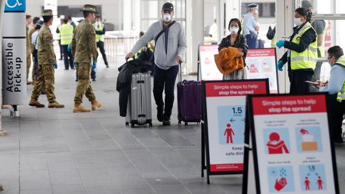 Returning overseas travellers walk towards waiting buses at Sydney Airport to take them to quarantine hotels.